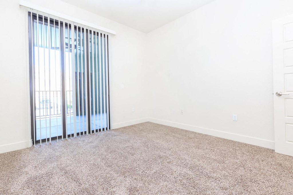 an empty living room with a sliding glass door to a balcony