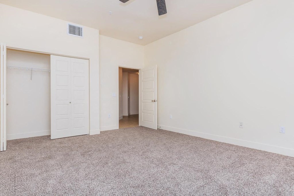 a bedroom with white walls and carpet and doors to a closet
