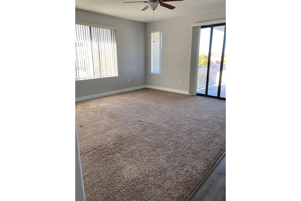 an empty living room with a ceiling fan and a sliding glass door