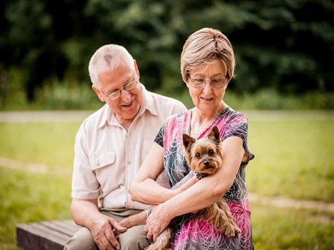 a man and woman sitting on a bench holding a small dog