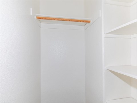 a walk in closet with white walls and a wooden shelf