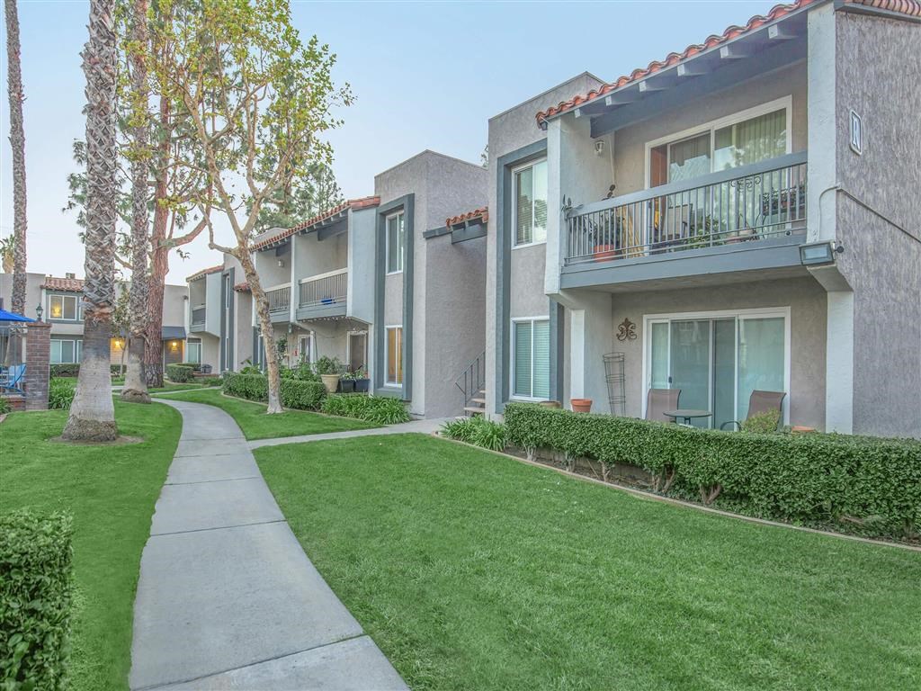 a sidewalk in front of an apartment building with grass and trees