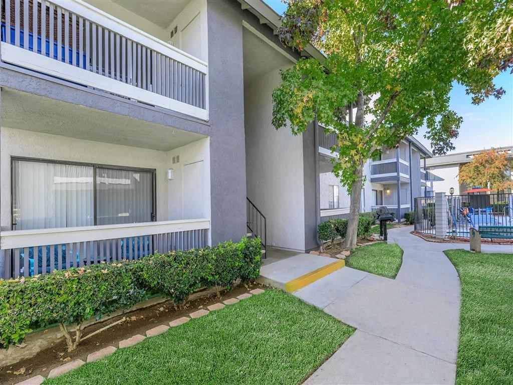 a sidewalk in front of an apartment building with grass and trees