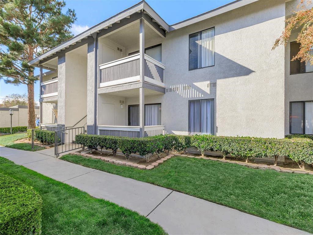 a sidewalk in front of an apartment building with grass