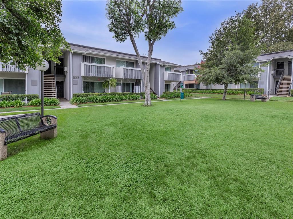 a grassy area with benches and trees in front of apartment buildings