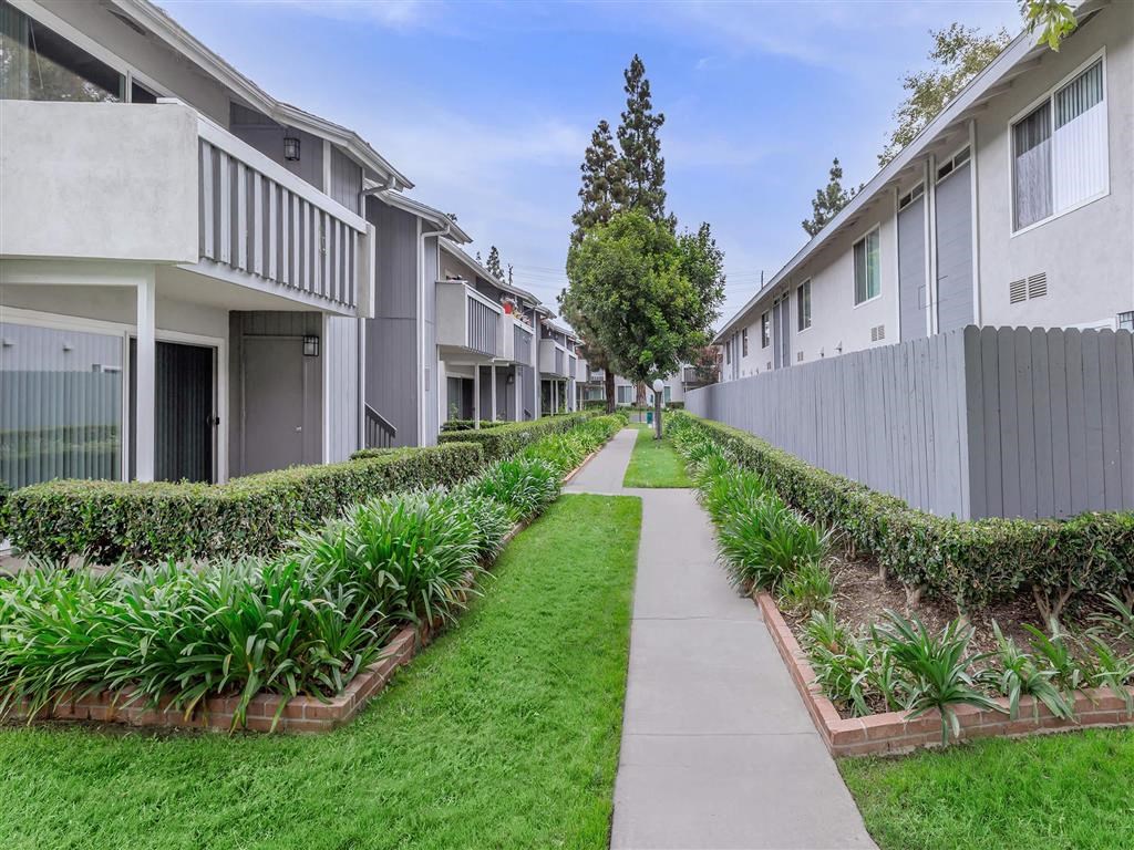 a sidewalk between two apartment buildings with grass and plants