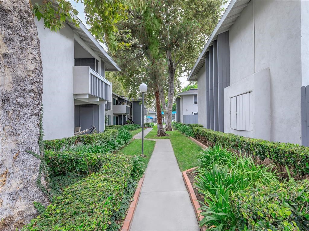 a sidewalk between two apartment buildings with trees and plants