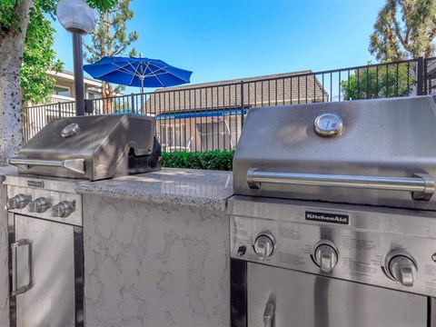 two stainless steel gas grills in a backyard with umbrellas