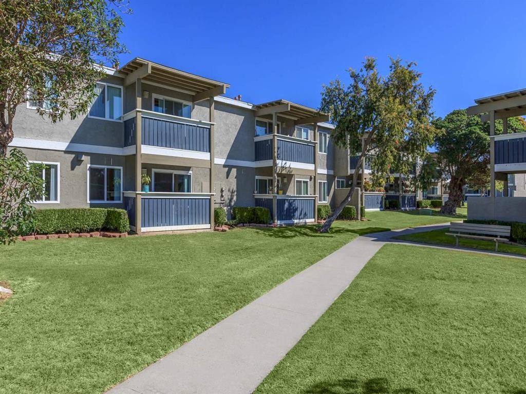 an exterior view of an apartment complex with a sidewalk and lawn