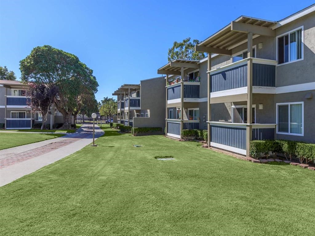 a grassy area between two apartment buildings and a sidewalk