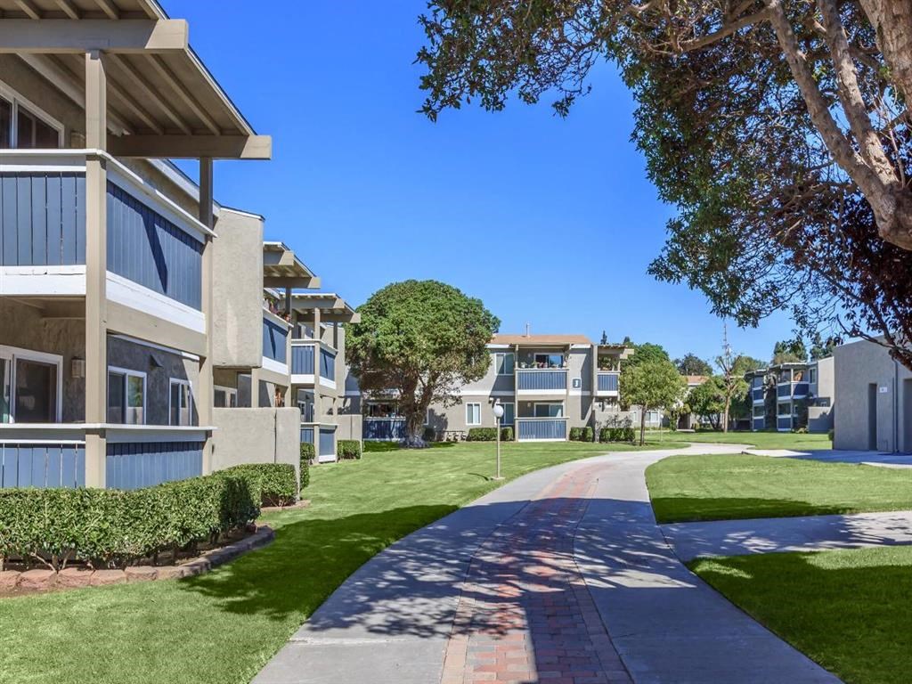a walkway between two apartment buildings with grass and trees