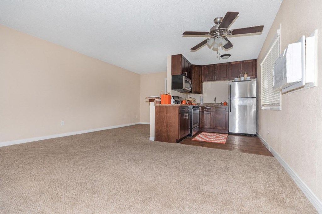 an empty living room with a kitchen with a ceiling fan