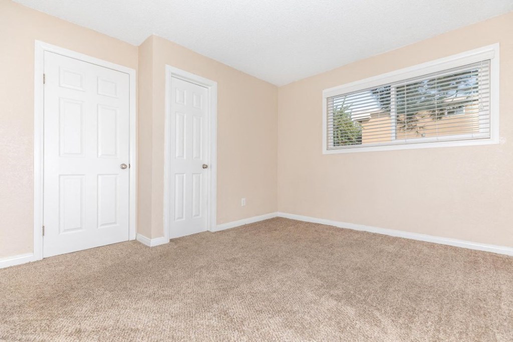 an empty bedroom with two doors and a window