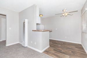an empty living room with a kitchen and a ceiling fan