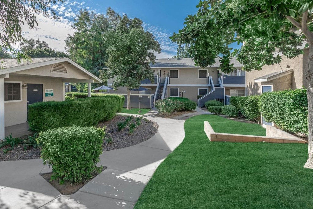 a walkway between two apartment buildings with trees and grass