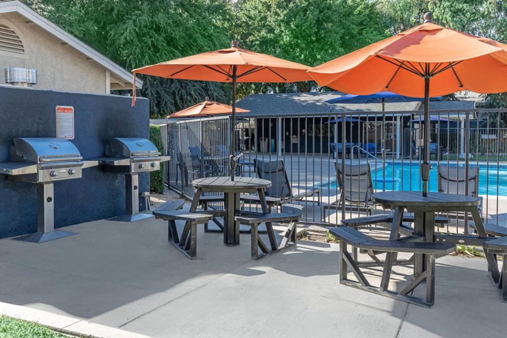 the patio has tables with umbrellas and chairs and a pool