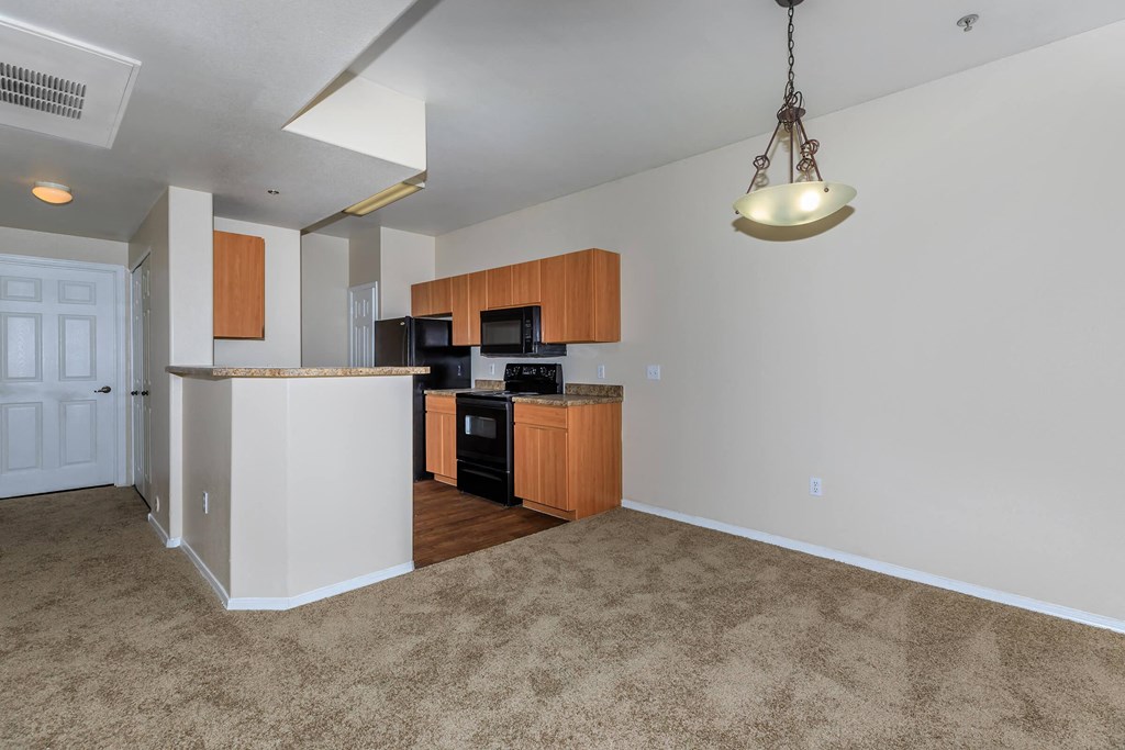 an empty living room with a kitchen with wood cabinets
