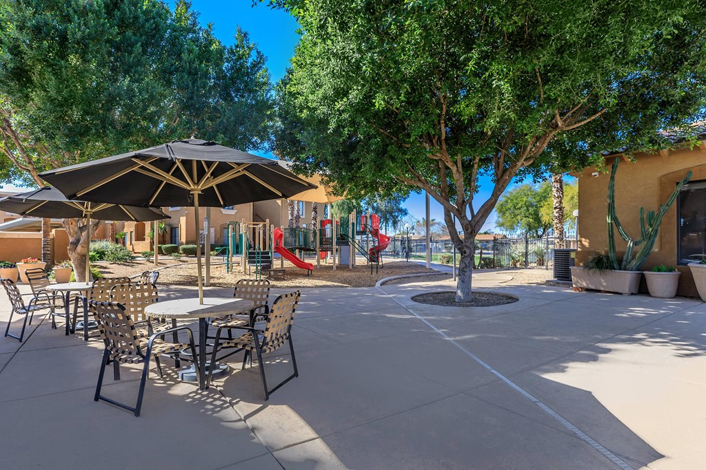 a patio with tables and chairs and trees and a playground