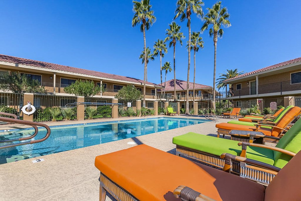 a swimming pool with orange and green lounge chairs      and buildings