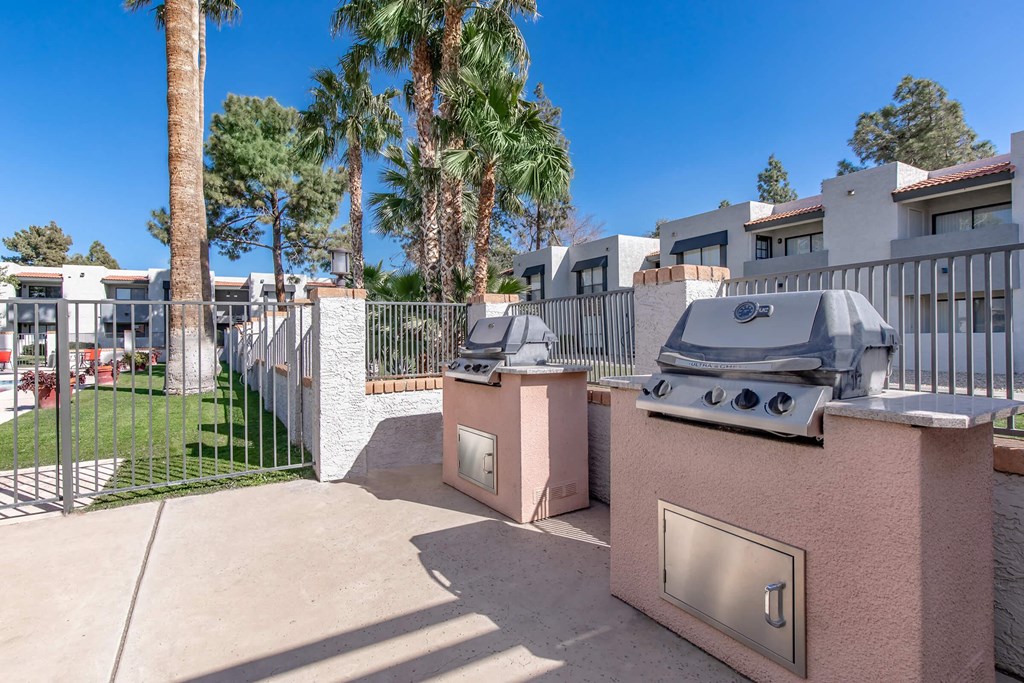 two barbecue grills in a backyard with a fence and palm trees