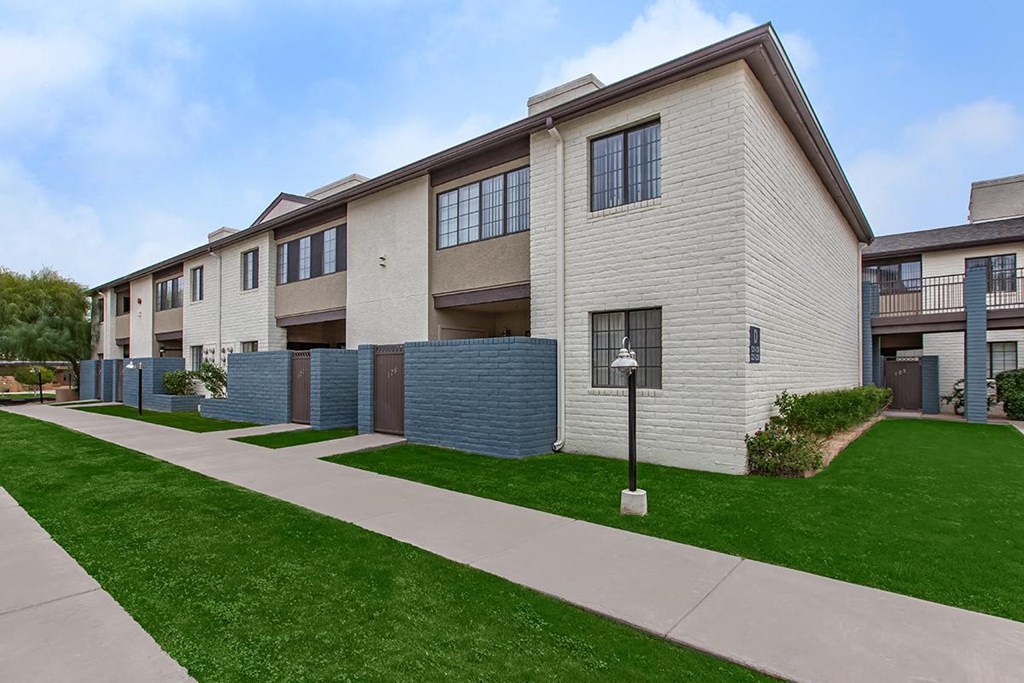 a row of apartments with a sidewalk and green grass