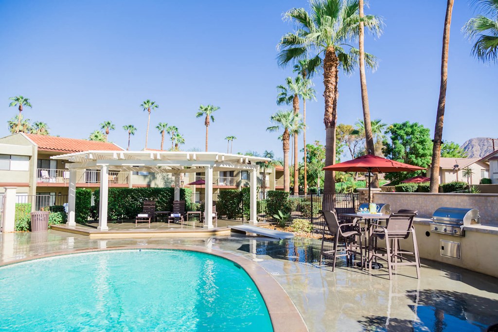 a resort style swimming pool with tables and chairs and palm trees