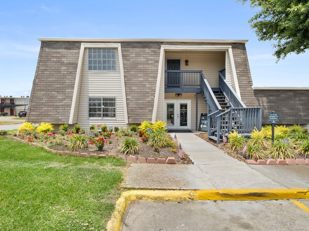the front of a building with stairs and a sidewalk and plants