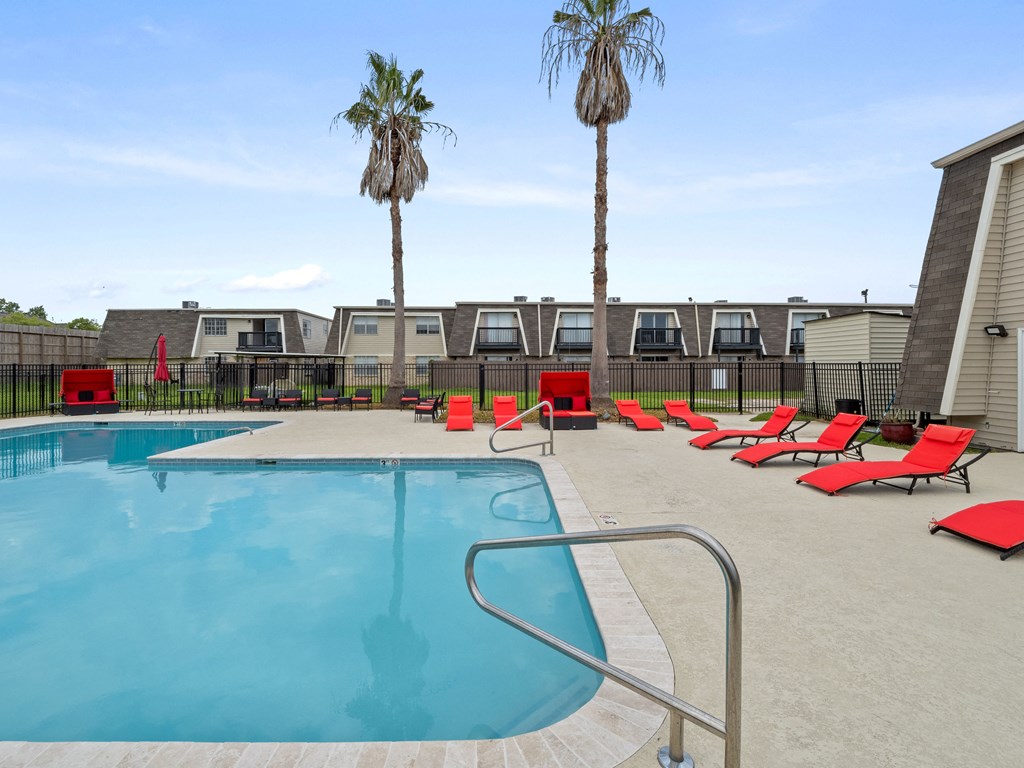 our resort style pool is filled with red lounge chairs and palm trees