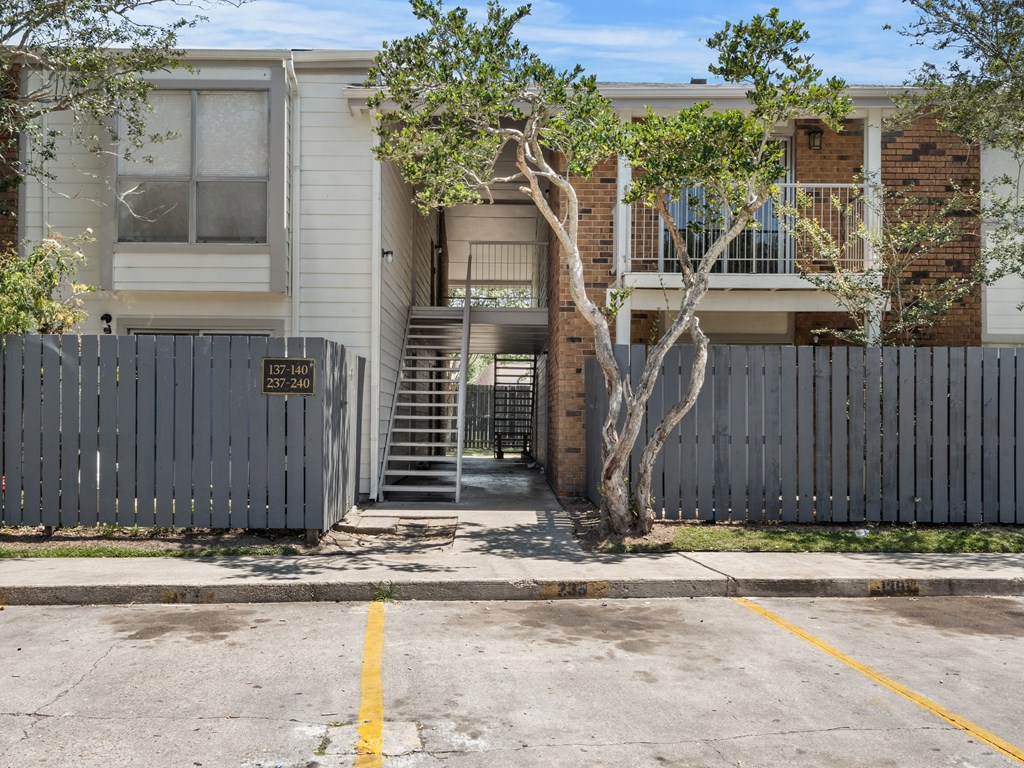 the front of an apartment building with a gate and a tree