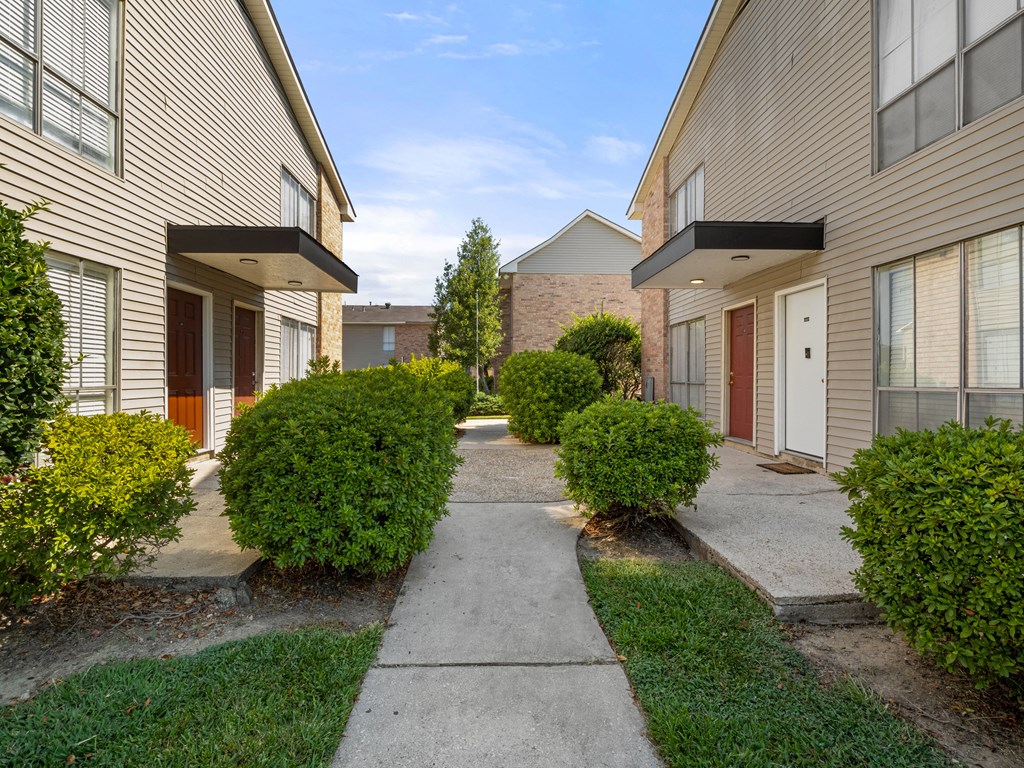 a walkway between two apartment buildings with grass and bushes
