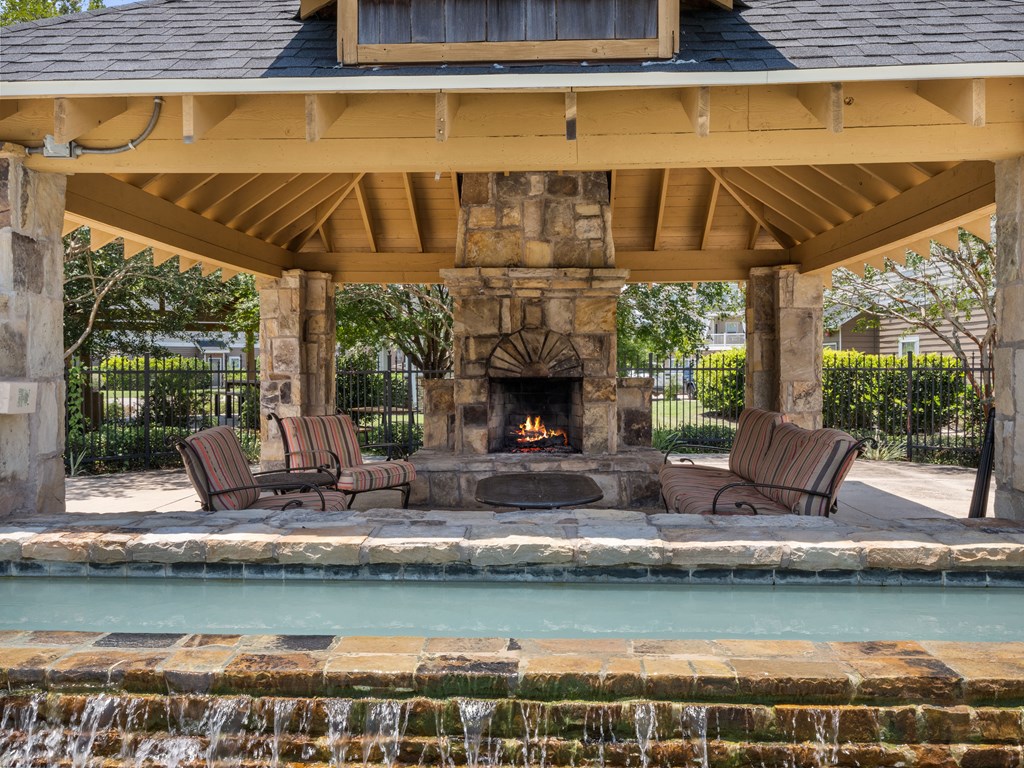 a pavilion with a fireplace and chairs next to a pool