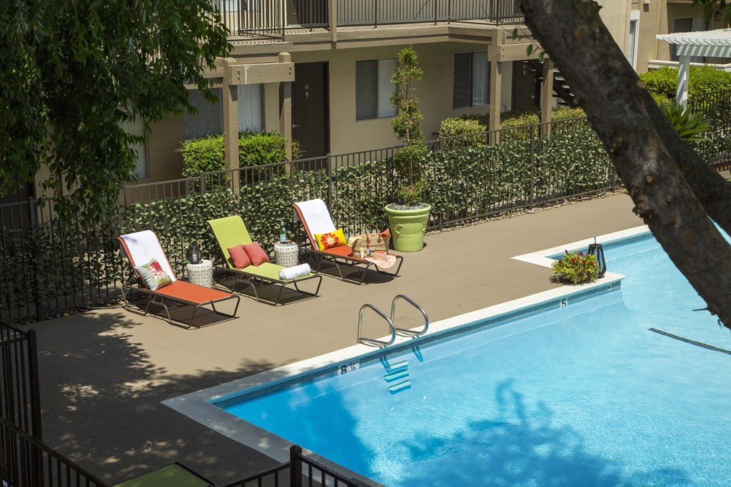 a swimming pool with lounge chairs and a tree in front of a building