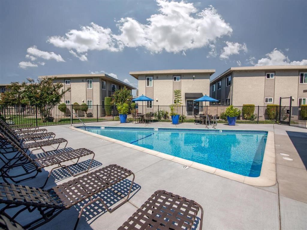 Community pool with lounge chairs, tables, and umbrellas with the community buildings behind it all
