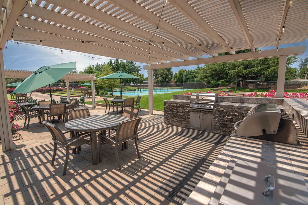 A covered patio with tables and chairs and a grill at Rivercrest Apartments, Sacramento 