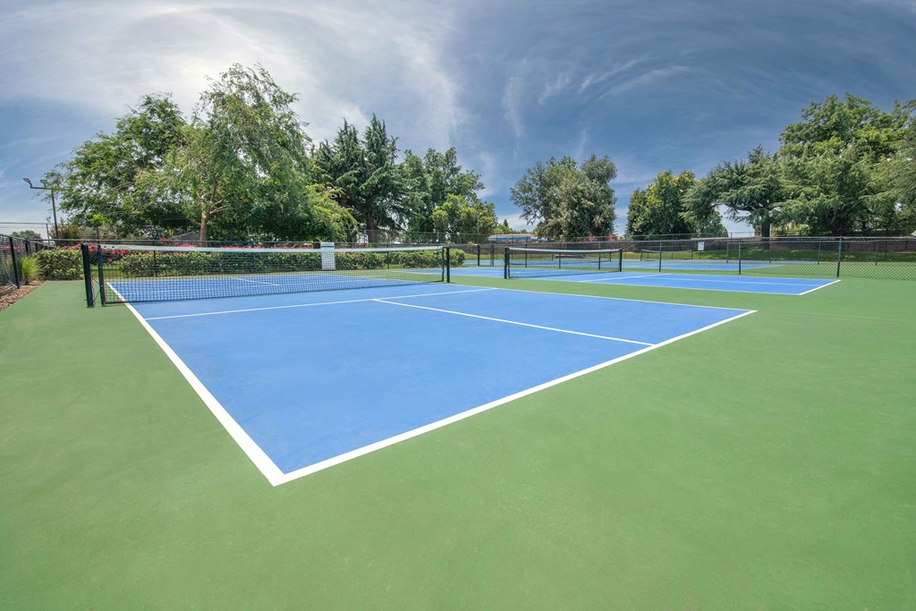 A blue and green tennis court with a net and trees at Rivercrest Apartments, Sacramento California 