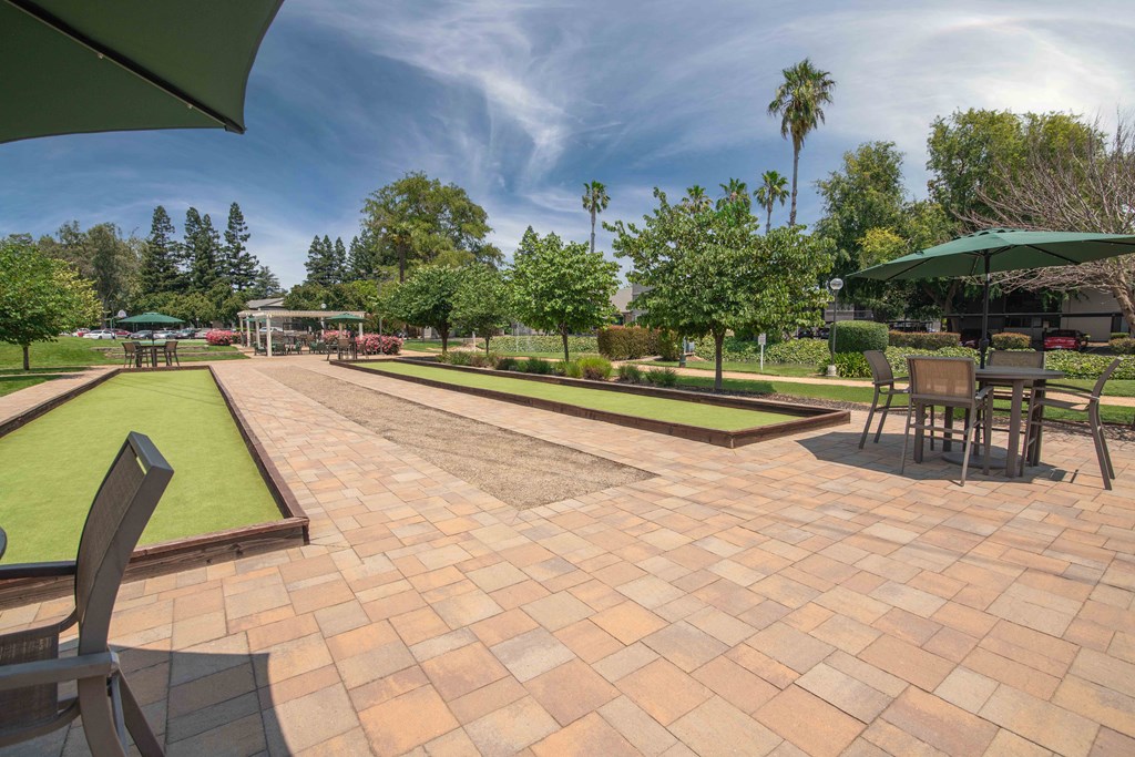 A large patio with tables and umbrellas and bocce call courts at Rivercrest Apartments, Sacramento 