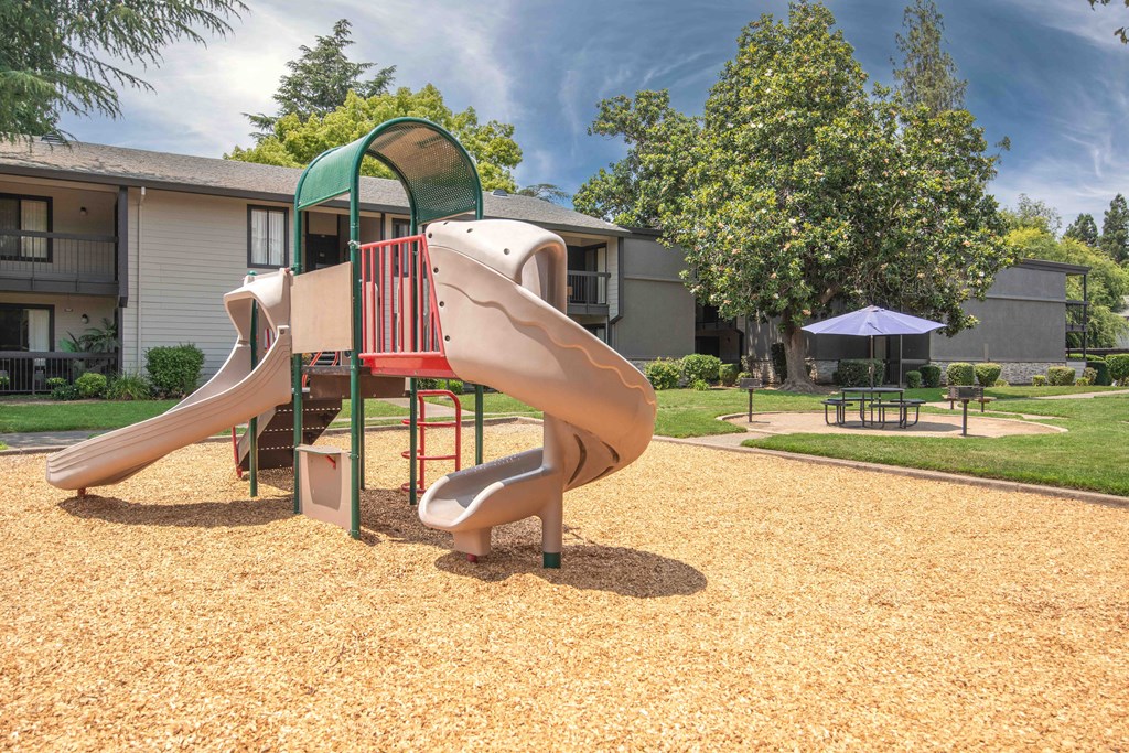 A playground with a picnic table and umbrella nearby at Rivercrest Apartments, Sacramento, 95826 