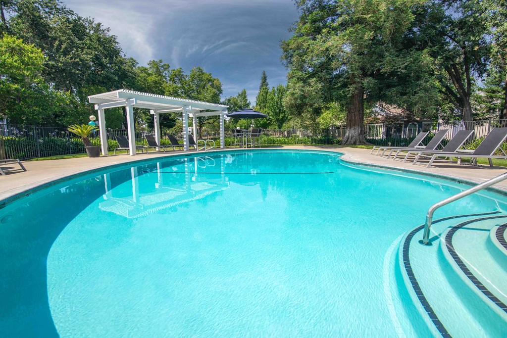 a large swimming pool with chairs and trees in the background at Willow Grove Apartments, California 