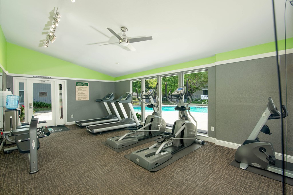 Fitness center with cardio equipment and windows overlooking a swimming pool at Willow Grove Apartments, Sacramento, CA 95825 