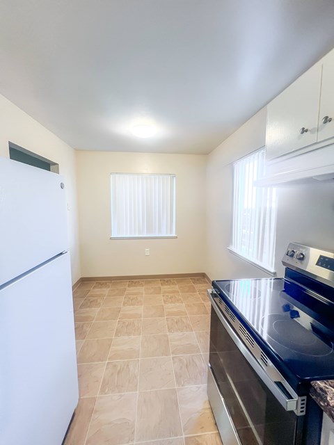 A kitchen with a white fridge, black stove and tiled floor.