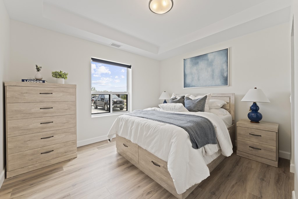 A bedroom with a large bed, a dresser, and a window overlooking a parking lot.