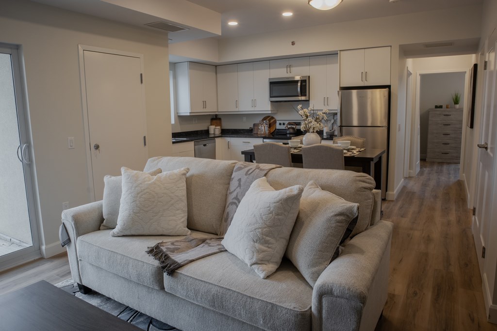 A living room with a grey couch and a kitchen in the background.