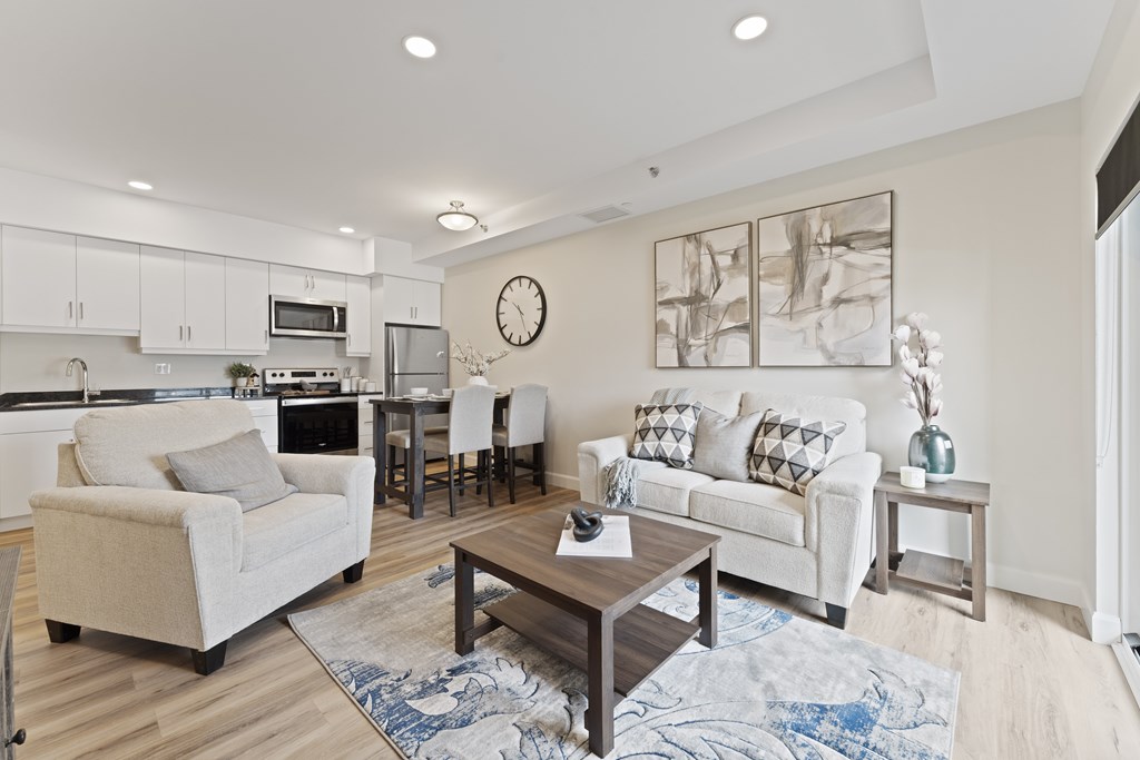 A modern living room with a white sofa, a beige armchair, a wooden coffee table, and a large abstract painting on the wall.