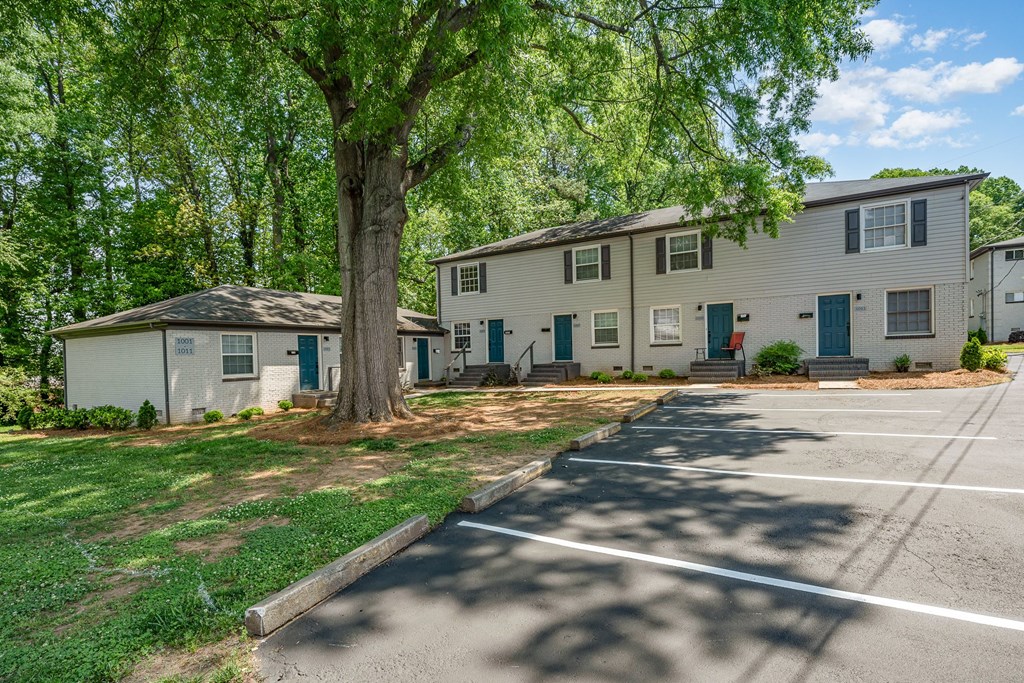 a white house with green doors and trees in a parking lot