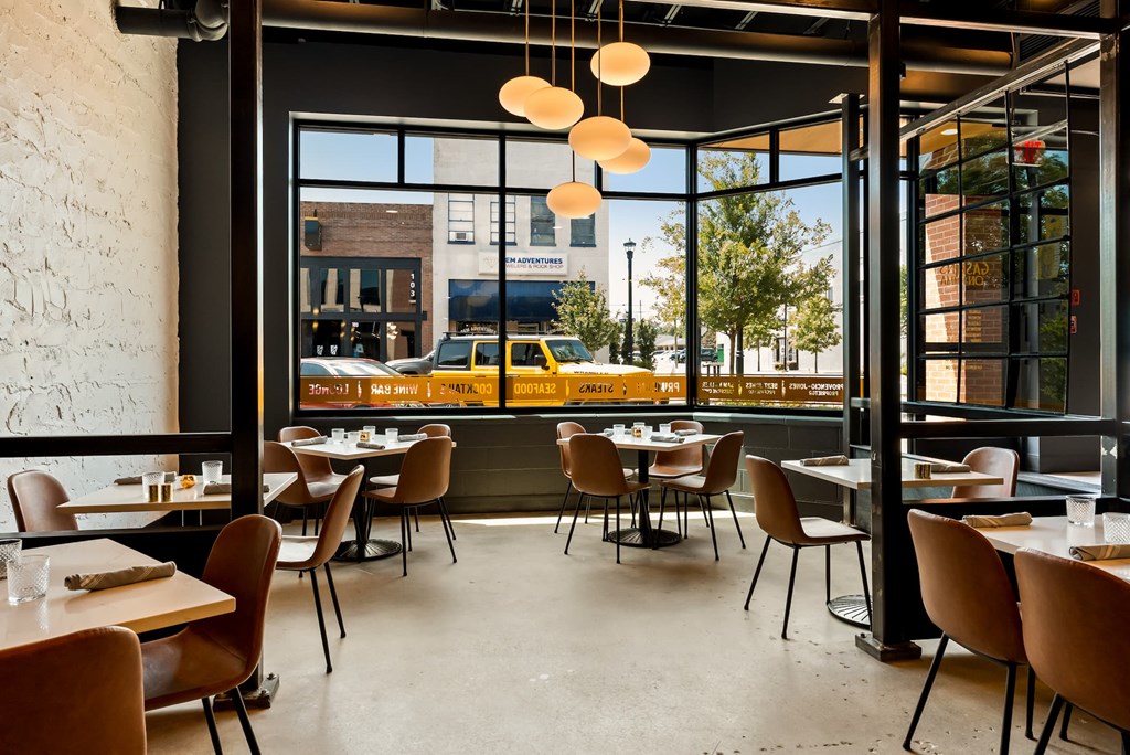 A restaurant with tables and chairs and a view of the street outside.