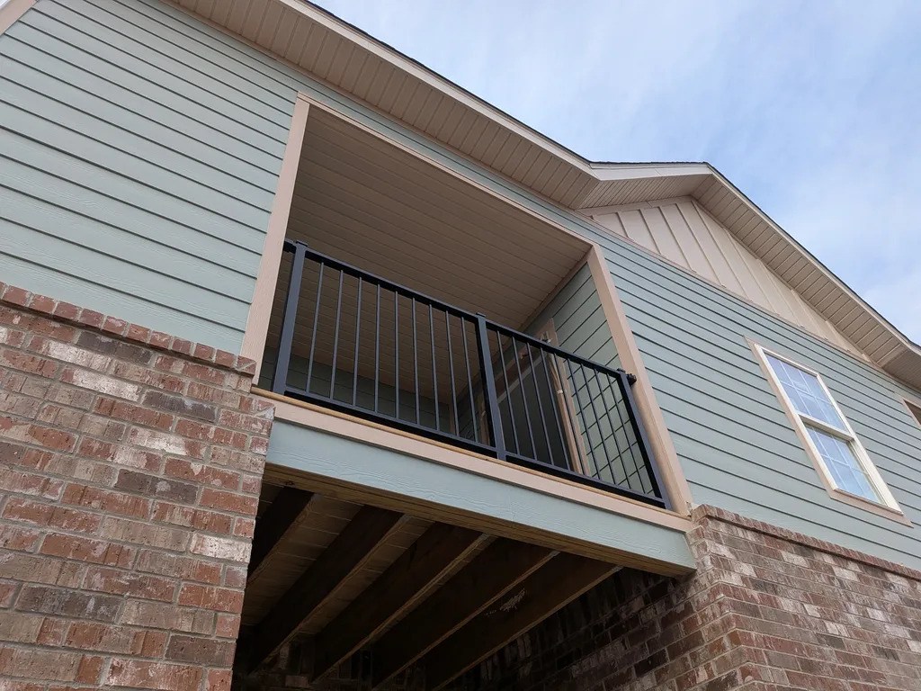 A balcony with a metal railing is attached to a brick building.