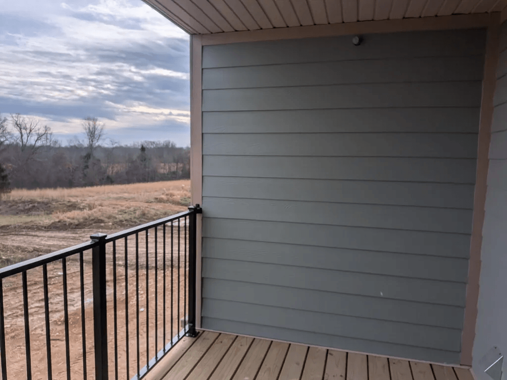 A balcony with a black railing and a grey wall.