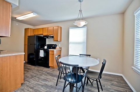 A kitchen with a black fridge and a dining table with four chairs.