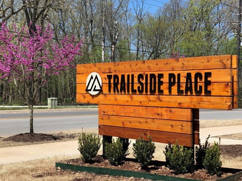 A wooden sign that says Trailside Place in front of a tree.