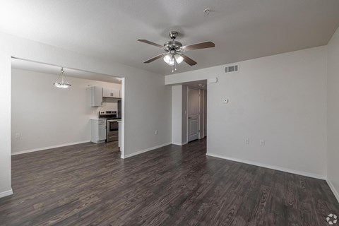 A room with a ceiling fan and a kitchen area in the background.